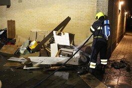 Brandweer blust stapel grofvuil tegen muur van flat