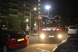 Brandweer blust stapel grofvuil tegen muur van flat